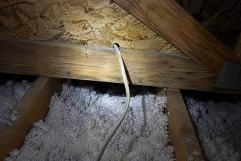 Nonmetallic sheathed cable pulled through a drilled hole in a wall top plate, seen from an attic over blown-in insulation