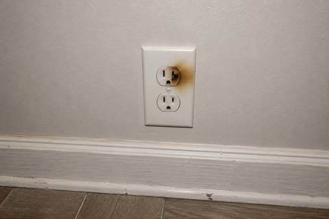 Wall receptacle with brown discoloration spreading from one slot across the faceplate, baseboard below