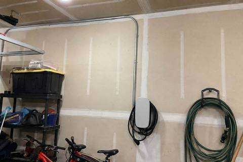 Electrical metallic tubing running along a garage ceiling and down a wall toward a mounted charging unit