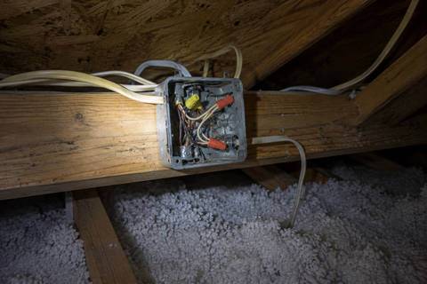 Junction box on an attic joist with the cover off, several cables entering it and connectors visible inside