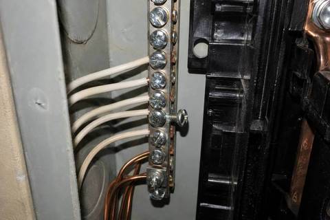 Neutral bar along the side of a panel enclosure with white conductors landed in its terminals, one screw backed out