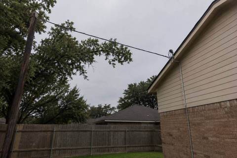 Overhead service drop running from a pole to a weatherhead on a house, tree branches close to the span