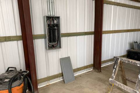 Small load center mounted on the interior wall of a metal building, cover off, breakers and feeder conductors visible