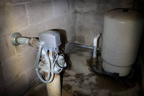 Pressure switch and wiring on a well head inside a small block pump house, pipework running out through the wall