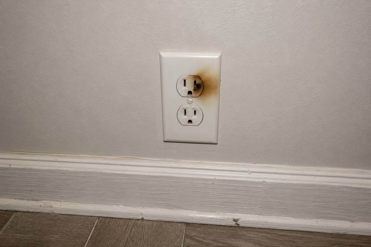 Wall receptacle with brown discoloration spreading from one slot across the faceplate, baseboard below