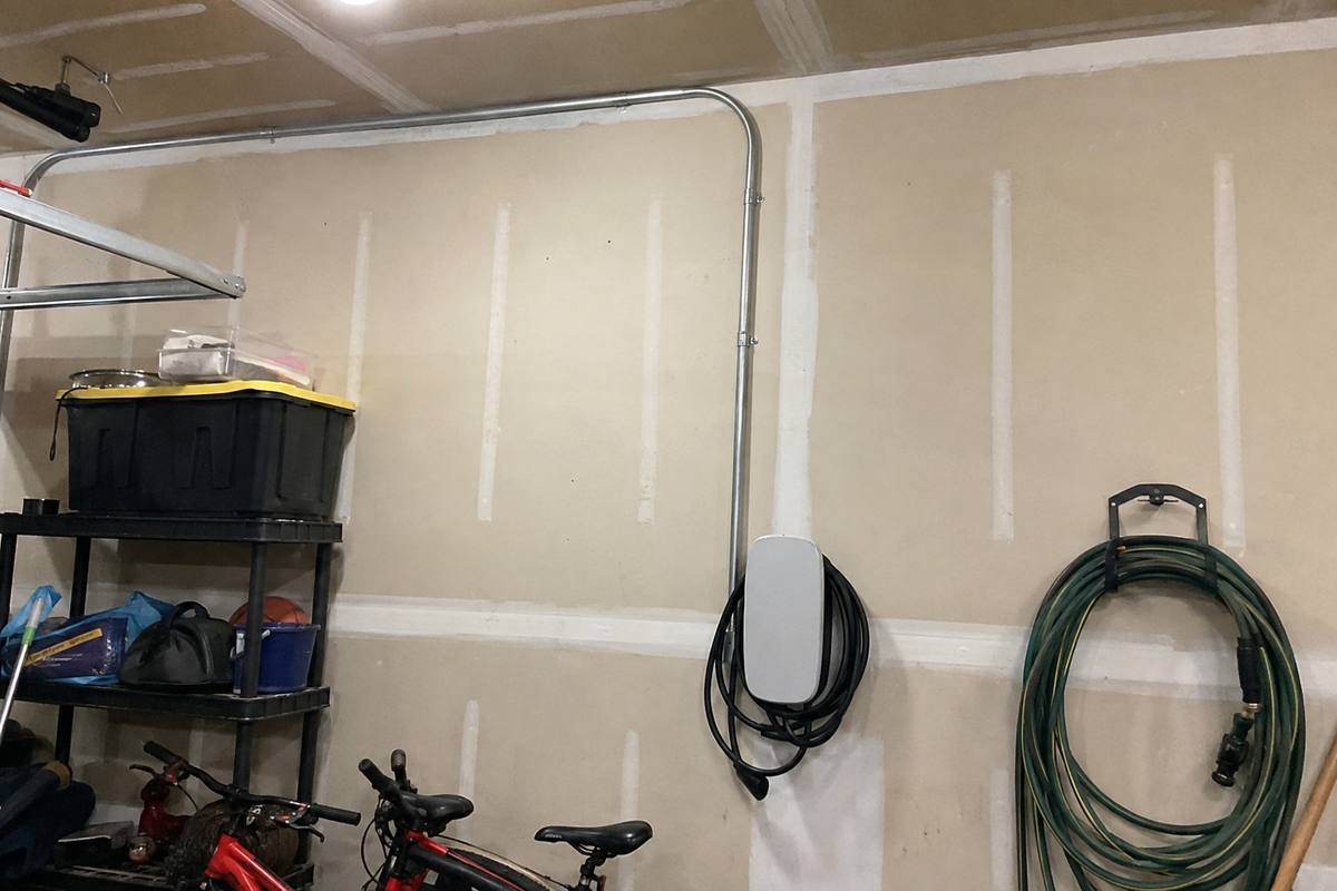 Electrical metallic tubing running along a garage ceiling and down a wall toward a mounted charging unit