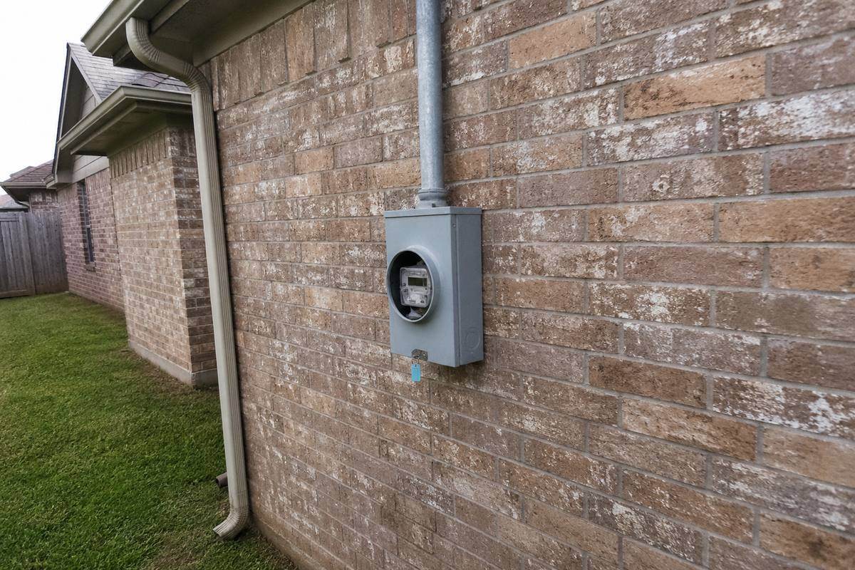 Meter base and service riser conduit mounted on the brick wall of a house, seal visible on the meter ring