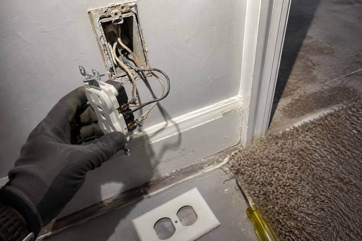 Receptacle pulled forward out of an old wall box with the conductors extended, faceplate on the floor below