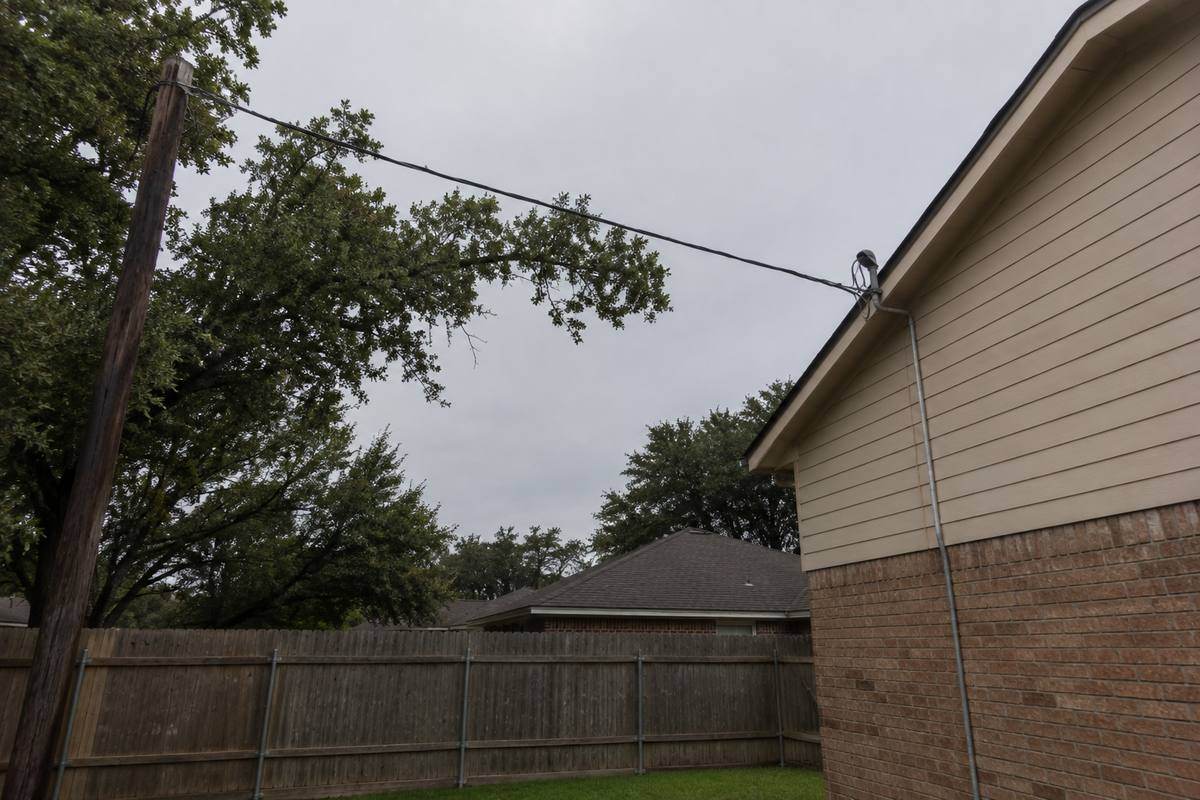 Overhead service drop running from a pole to a weatherhead on a house, tree branches close to the span